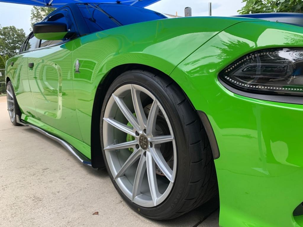 Close-up of a green sports car with large alloy wheels parked on a concrete surface.