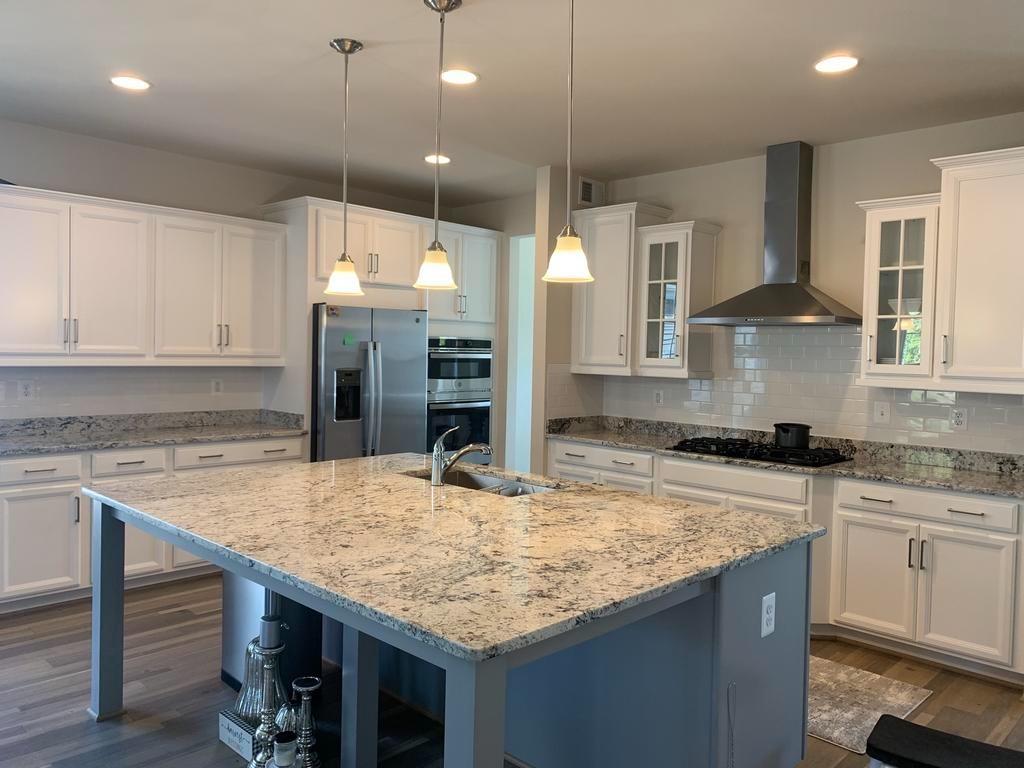 Modern kitchen with white cabinets, stainless steel appliances, large island with granite countertop, and pendant lighting.