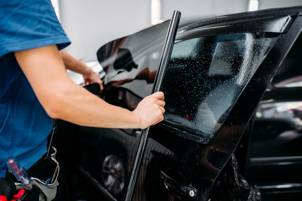 Person applying a tint film to a car window with tools on their waist.