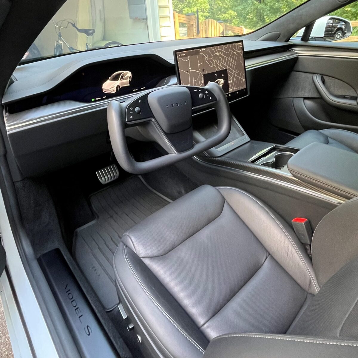 Interior of a Tesla vehicle showing the steering wheel, dashboard with digital displays, and front seats in a sleek, modern design.