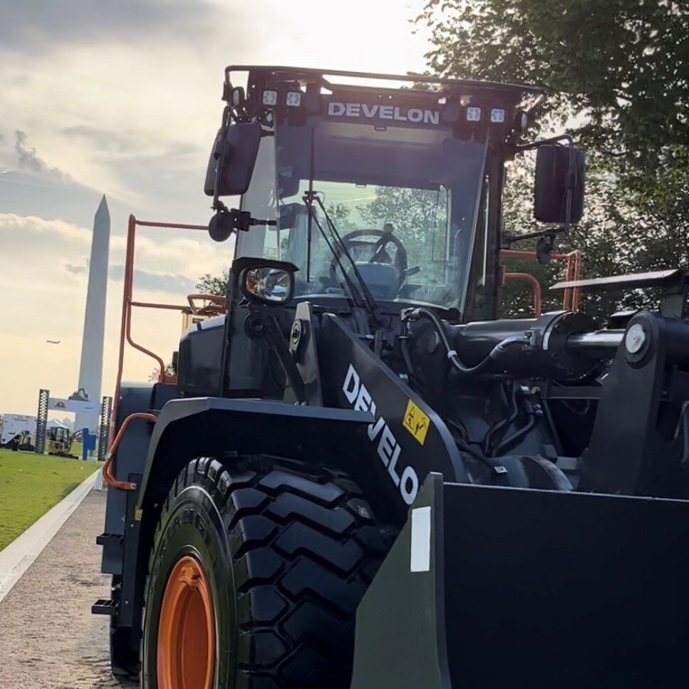 Front view of a Develon construction vehicle parked on a road with the Washington Monument visible in the background.