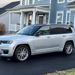 A silver SUV is parked on a driveway in front of a blue and white two-story house with a garage.