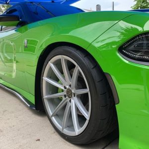 Close-up of a green sports car with large alloy wheels parked on a concrete surface.