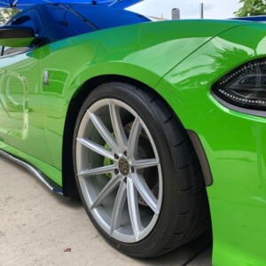 Close-up of a green sports car with large alloy wheels parked on a concrete surface.