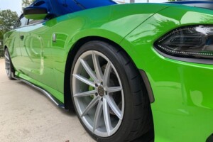 Close-up of a green sports car with large alloy wheels parked on a concrete surface.